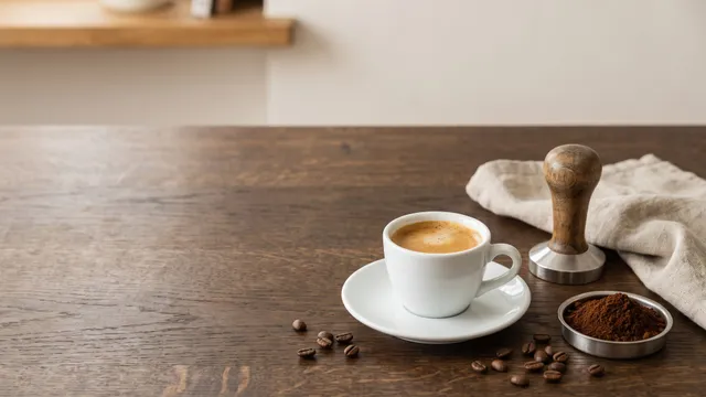 KI-generiertes Symbolbild: Espressotasse mit Crema, Handtamper aus Holz und eine Schale mit gemahlenem Kaffee auf dunkler Holzplatte